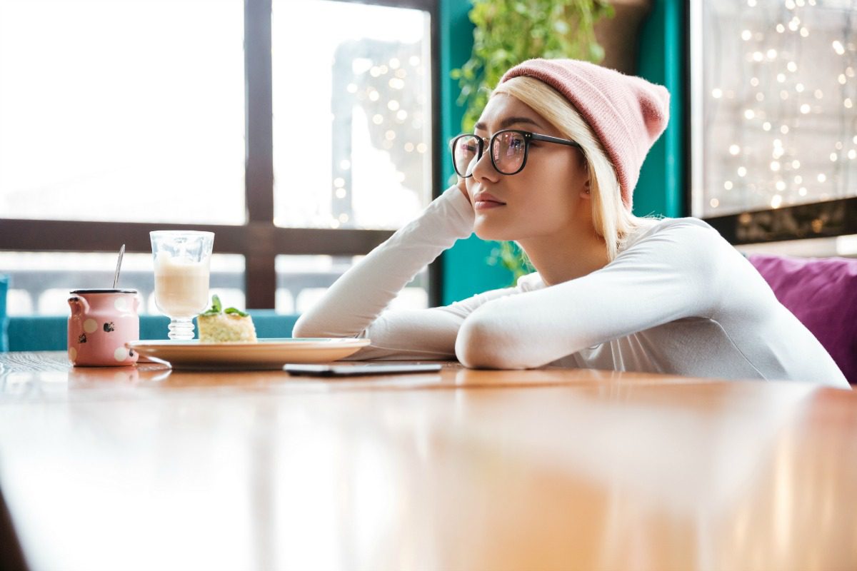 graphicstock sad bored young woman in hat and glasses sitting at the table in cafe BkZblYO0al