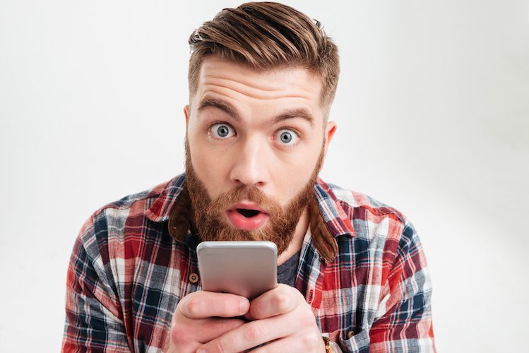 graphicstock close up portrait of a surprised bearded man holding phone and looking at camera with eyes wide open over white background H U8rH7Pnl